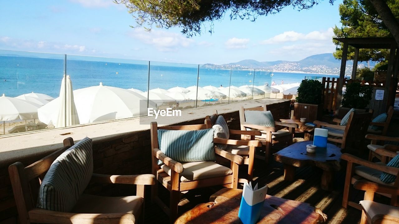 Empty chairs and tables at restaurant by sea against sky