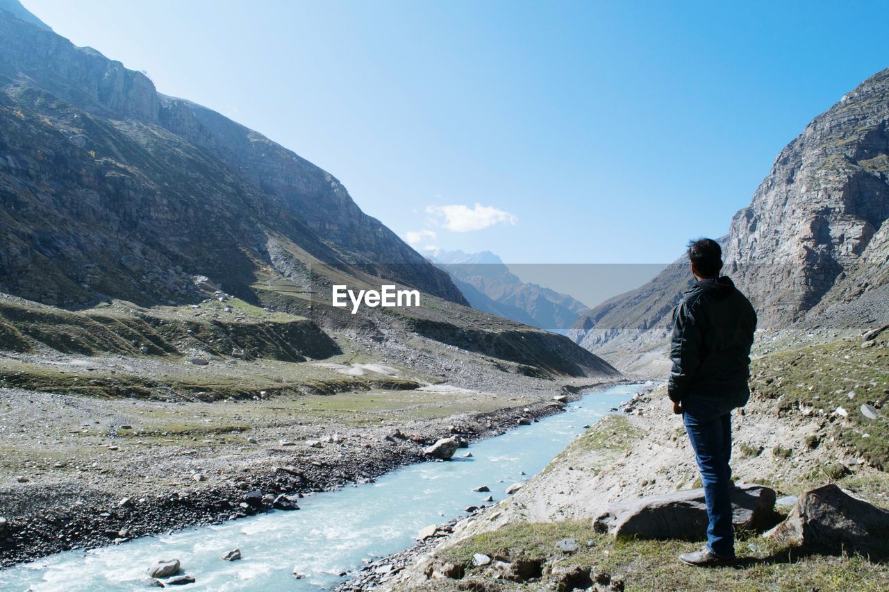 Man standing by river against mountain range