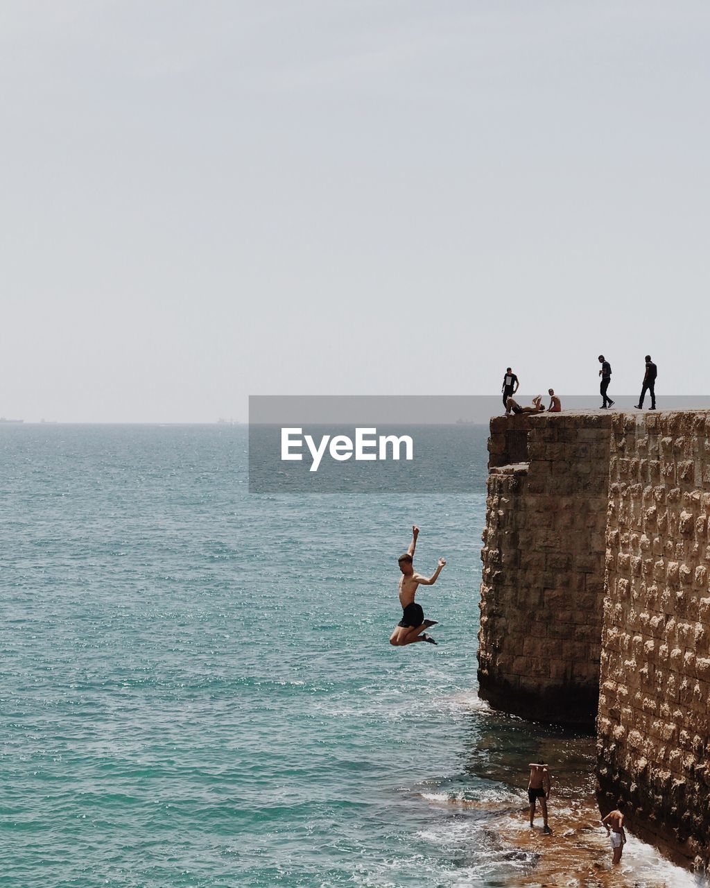 PEOPLE STANDING ON SHORE AGAINST CLEAR SKY