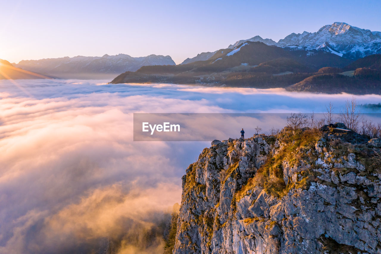 High angle view of man standing on mountain ridge rising above the clouds, hallein, austria