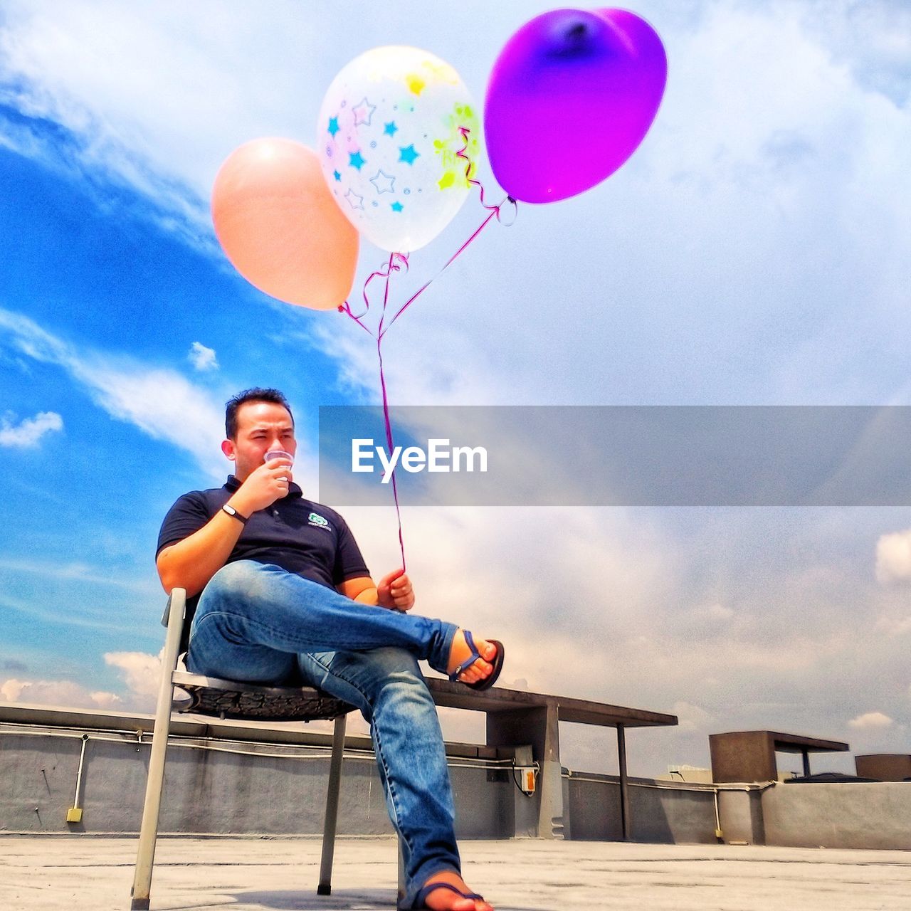 LOW ANGLE VIEW OF MAN SITTING ON BALLOONS
