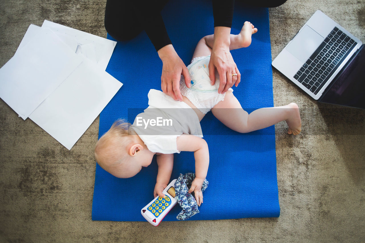 High angle view of working mother caring daughter on exercise mat at home