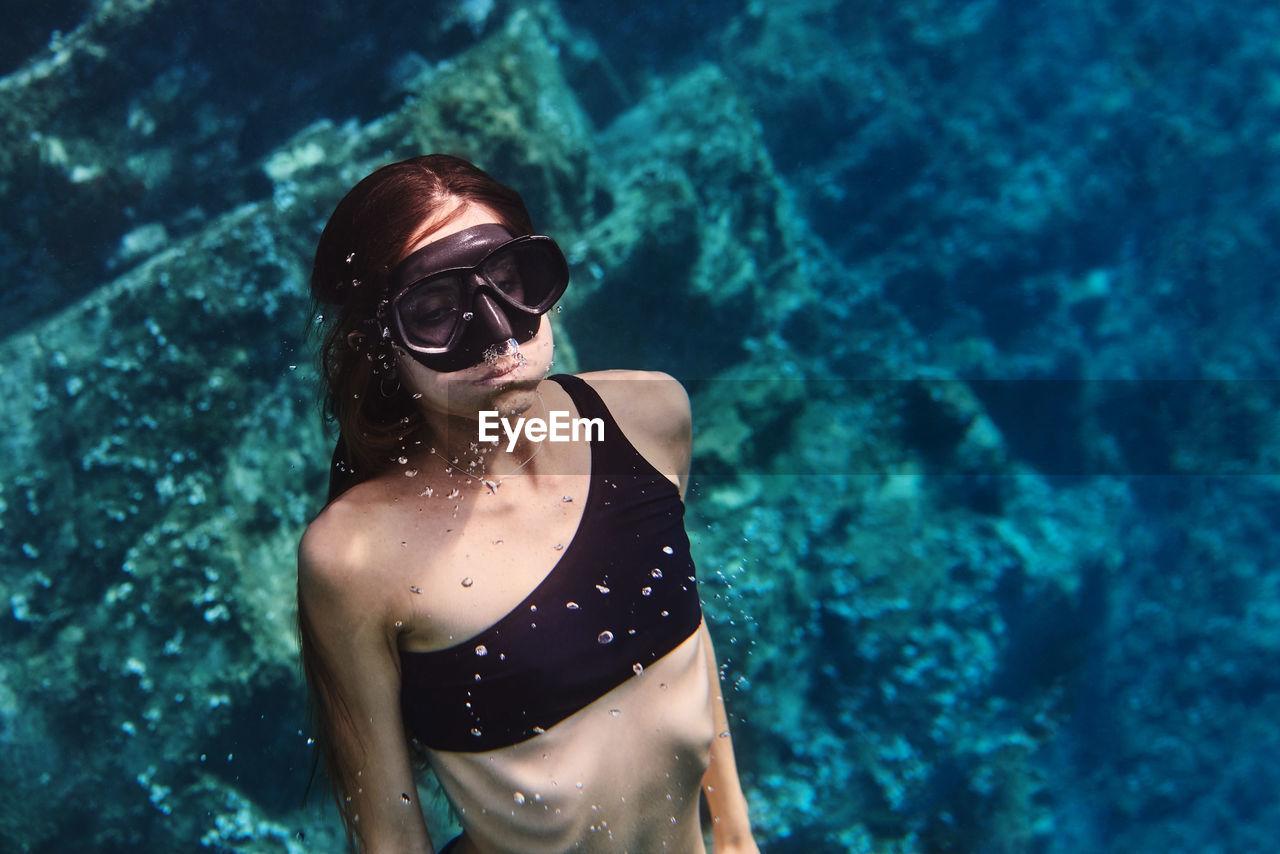 Young female diver in swimsuit and snorkeling mask floating in clean transparent sea water