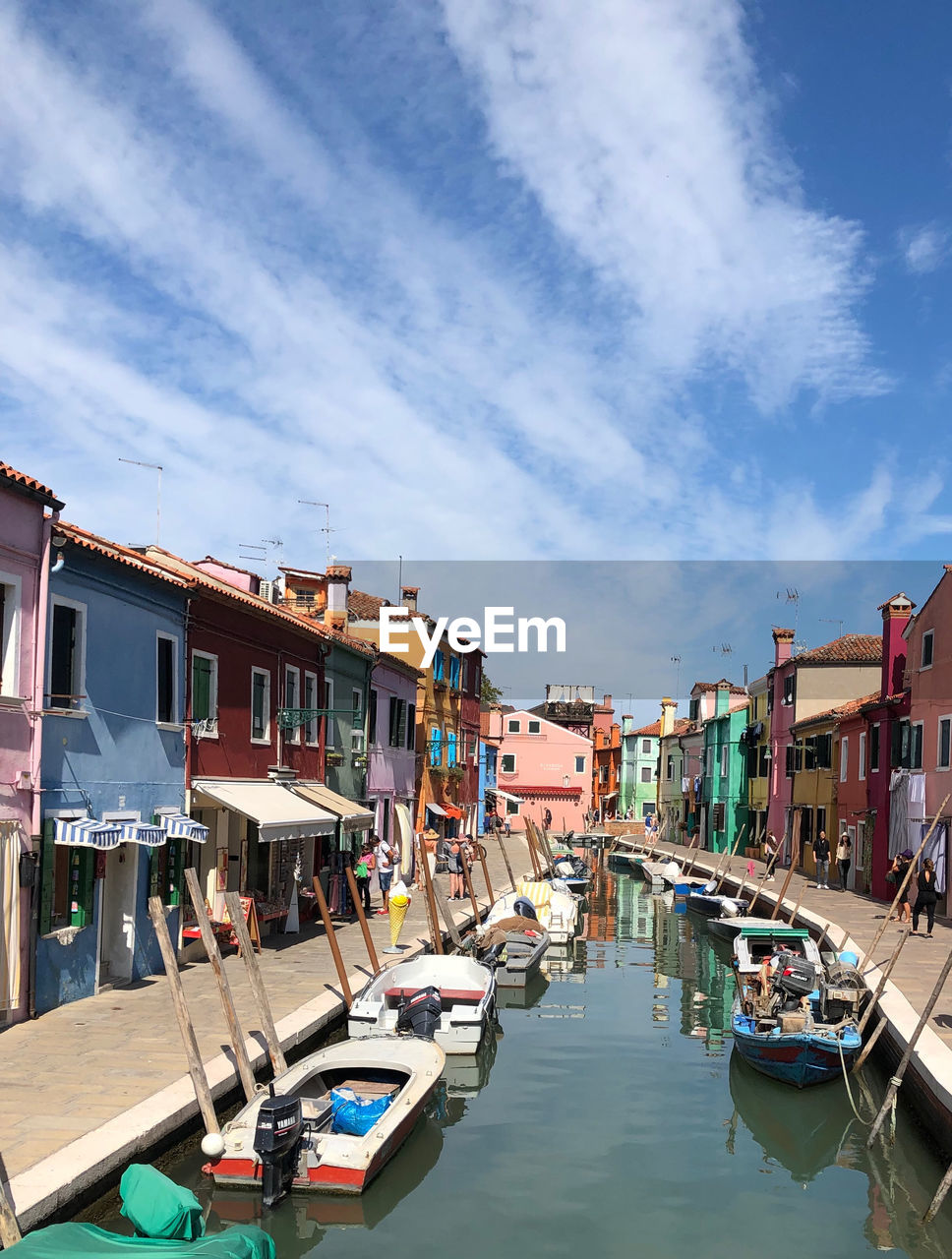 Boats moored in canal amidst buildings in city against sky