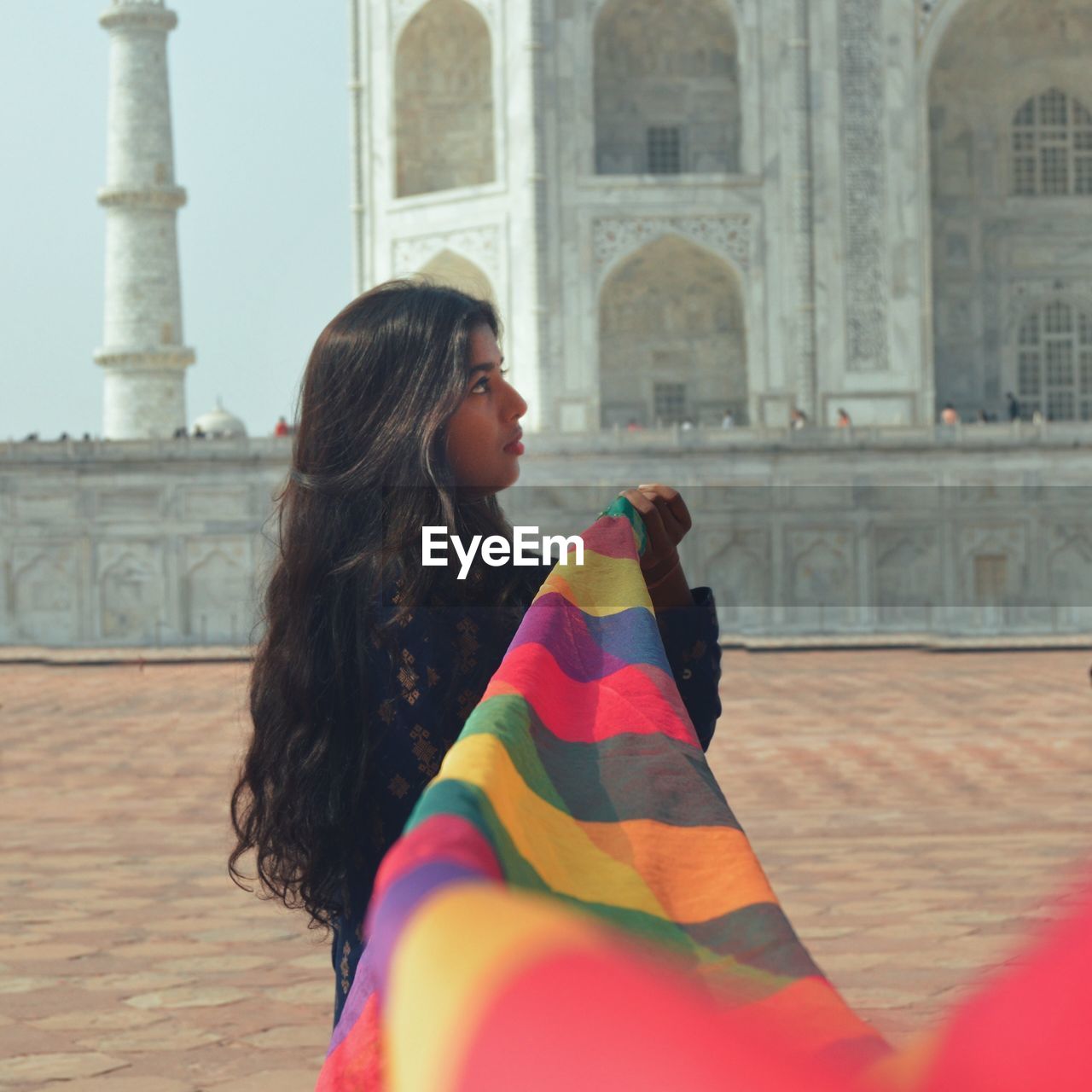 Woman holding colorful scarf in front of taj mahal