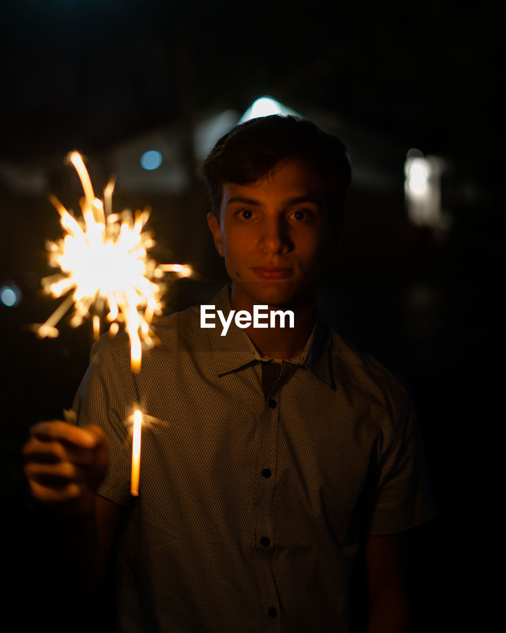 Portrait of young man holding illuminated sparkler at night