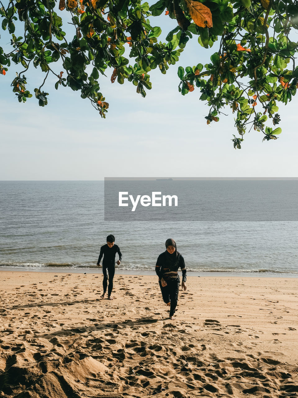 Two friends running towards the camera on the beach on a sunny day