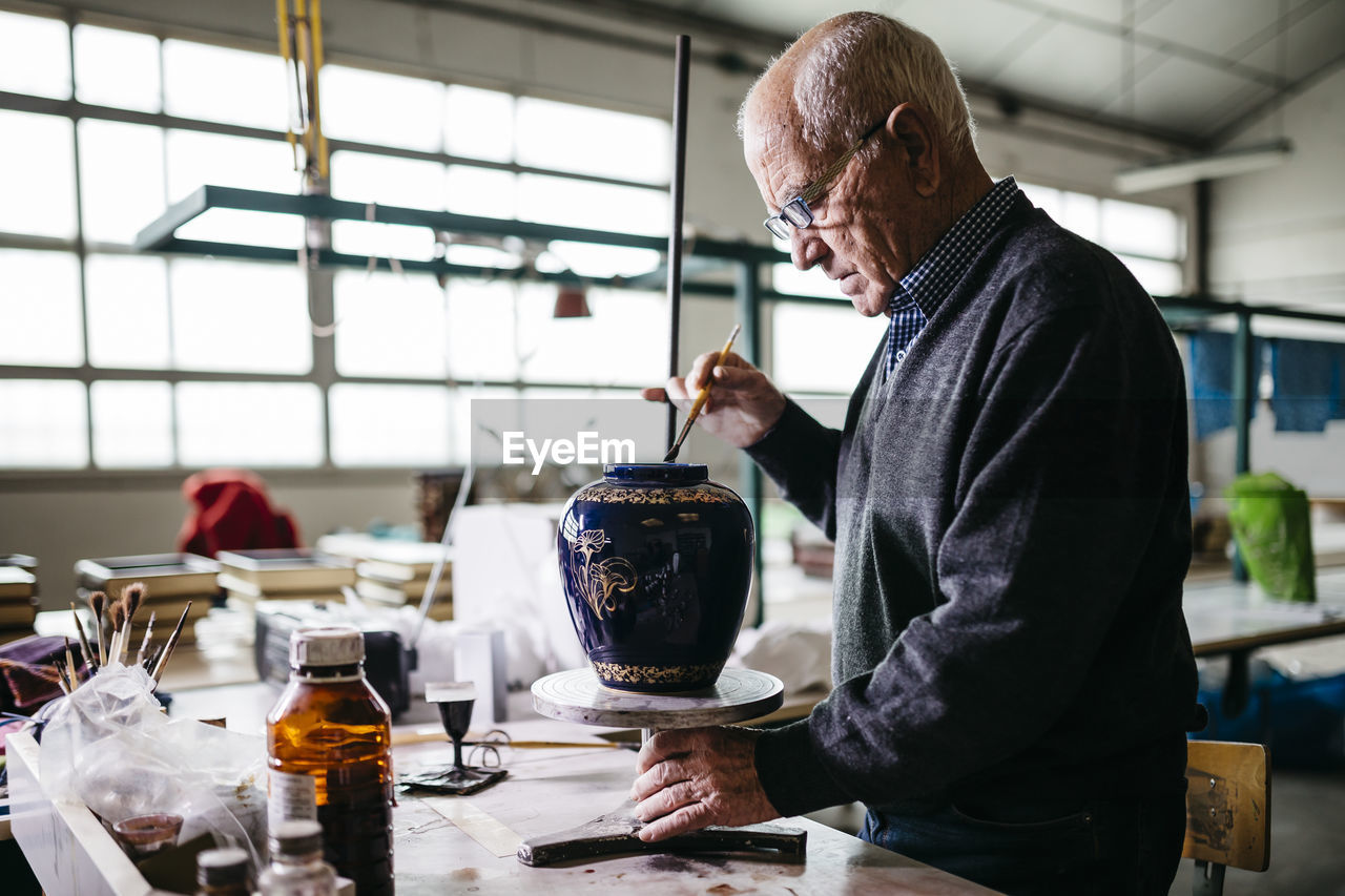 Senior man decorating ceramic vase in his spare time