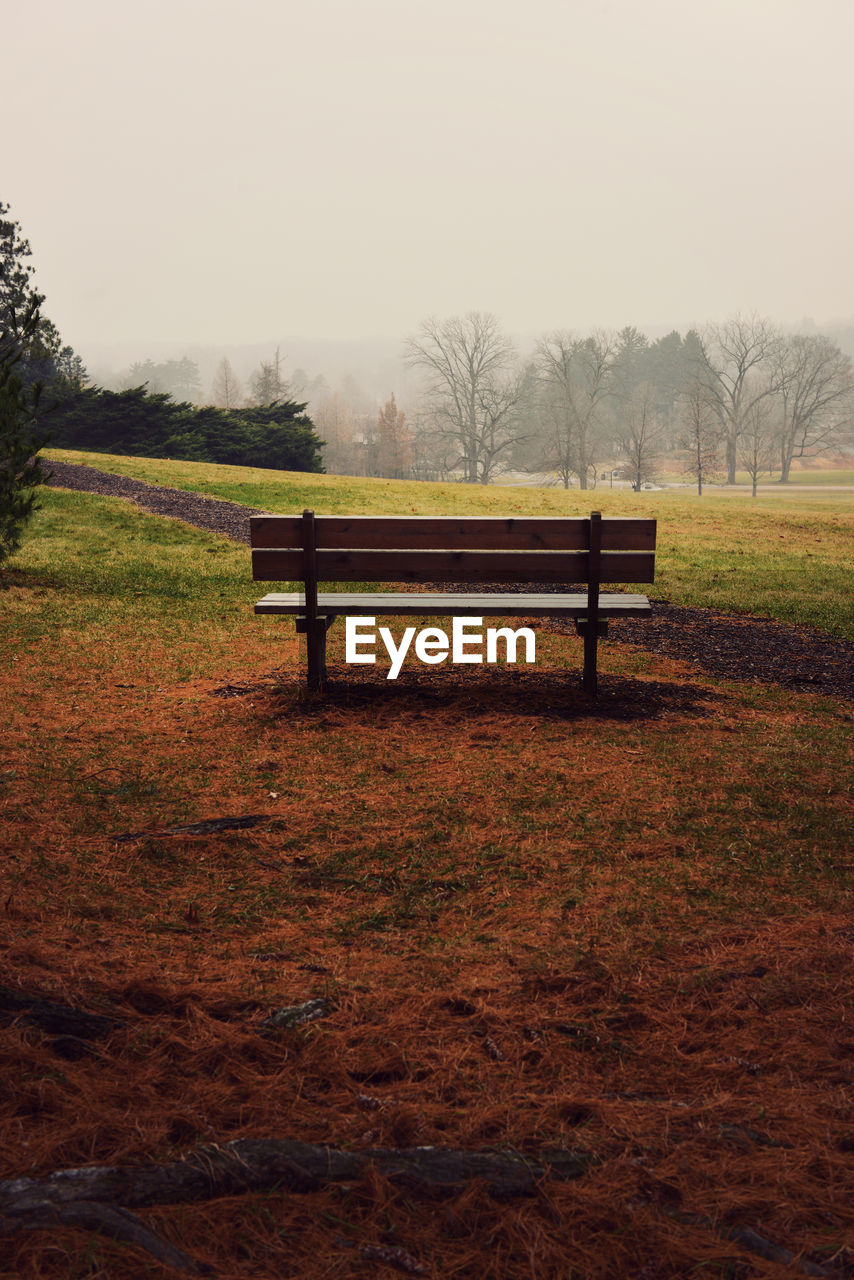 Empty bench on field against sky