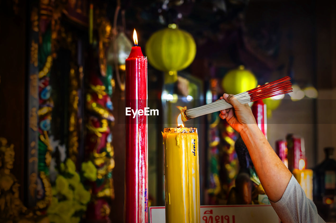 Cropped hand of person lighting incense sticks at temple