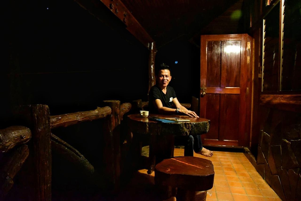 Portrait of man sitting on chair by table in darkroom