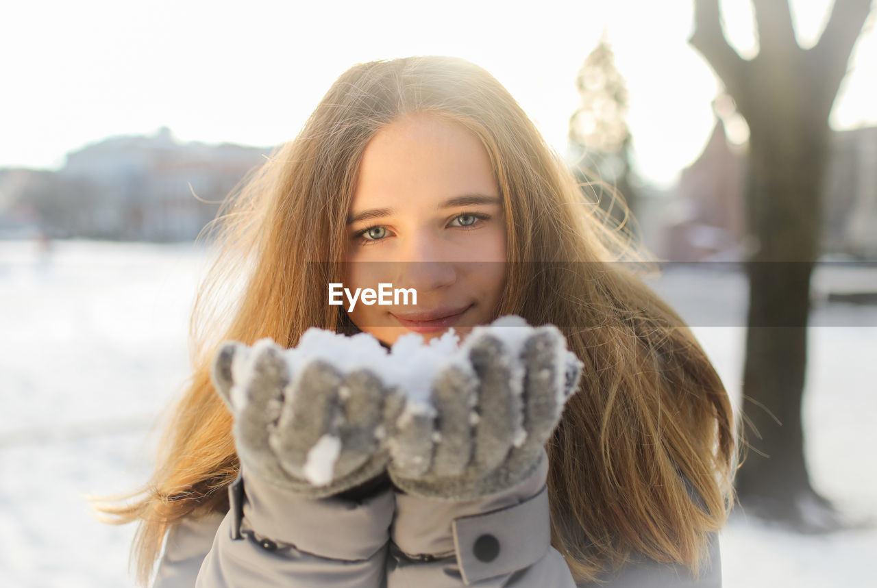 Portrait of smiling young woman holding snow in winter