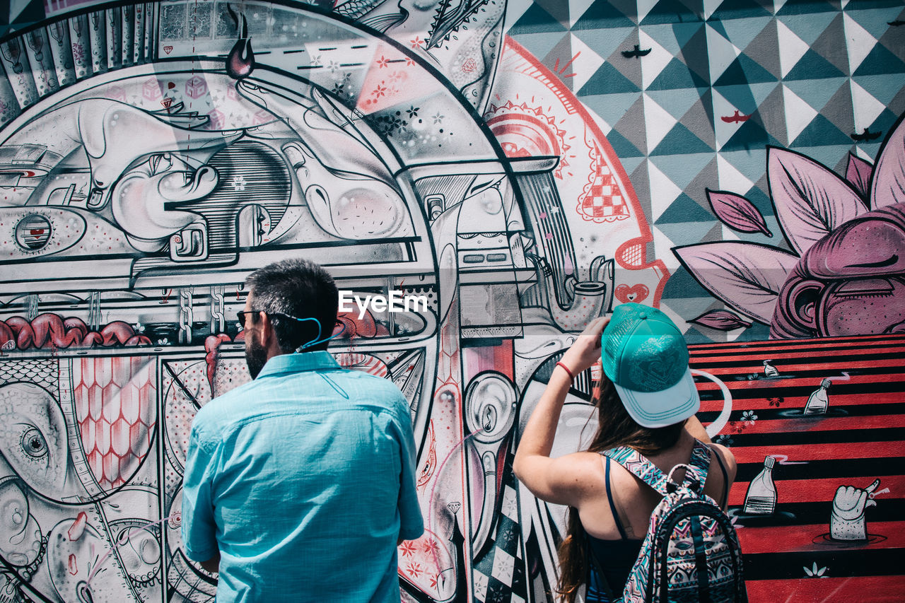 REAR VIEW OF MAN AND WOMAN STANDING AGAINST GRAFFITI