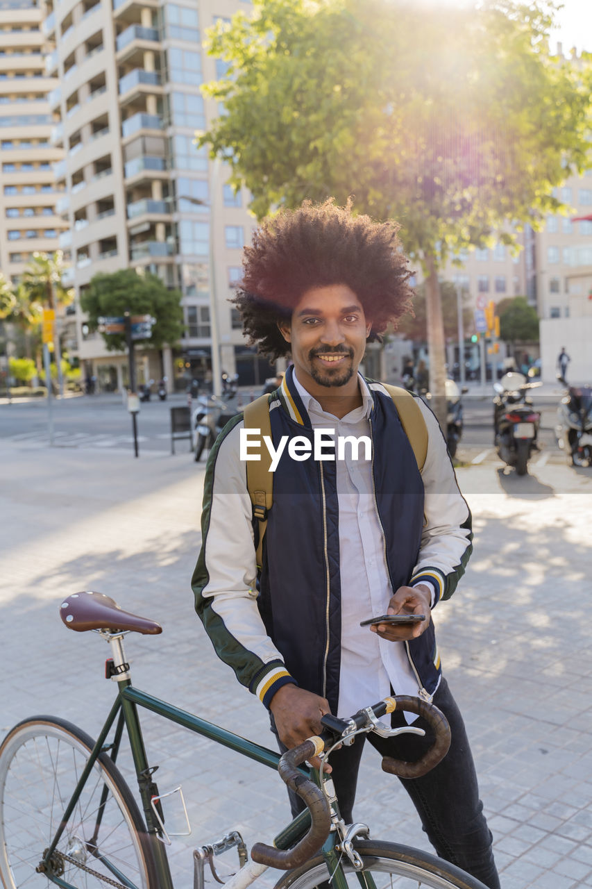 Portrait of smiling casual businessman with bicycle and cell phone in the city, barcelona, spain