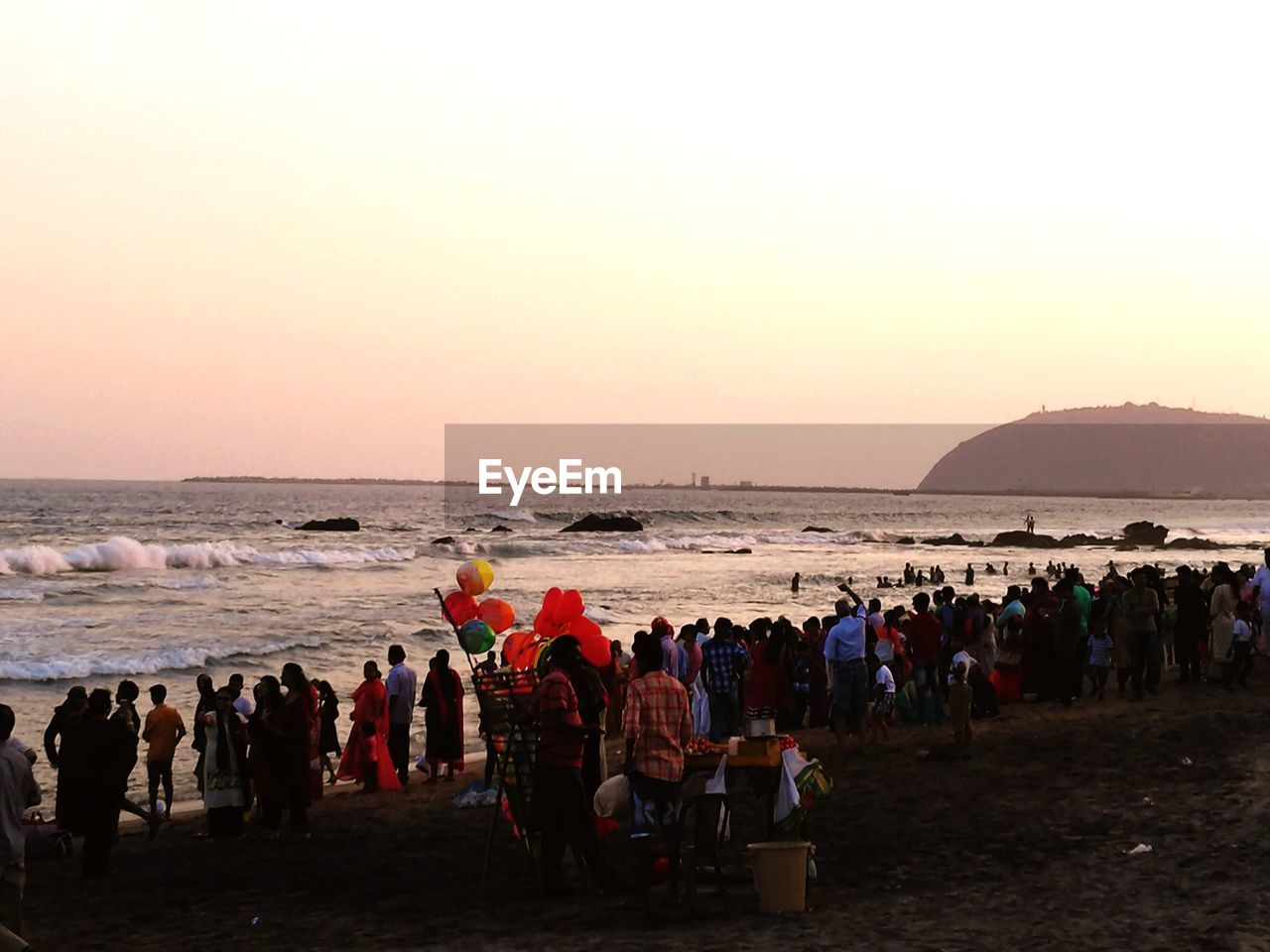 People at beach against clear sky during sunset