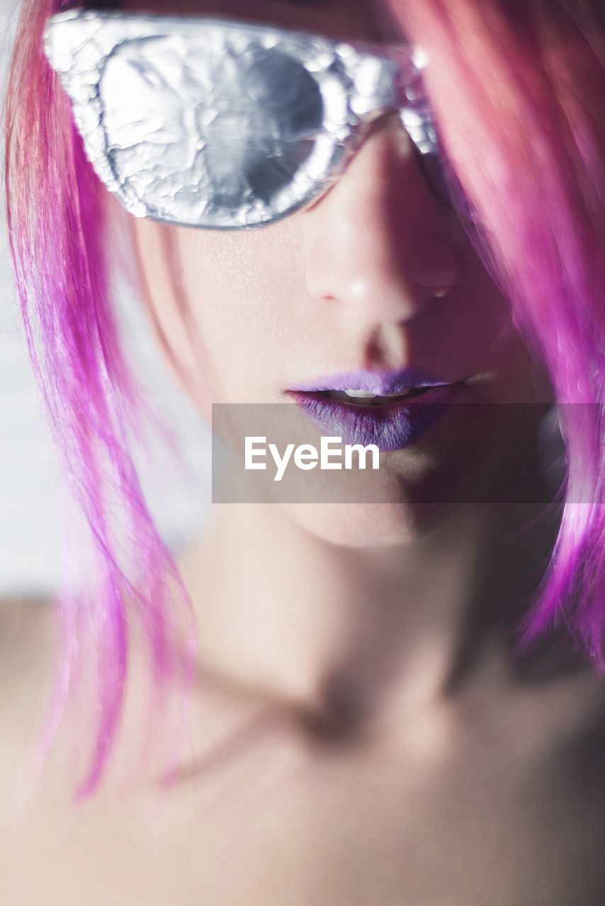 Close-up portrait of topless young woman with purple hair wearing sunglasses