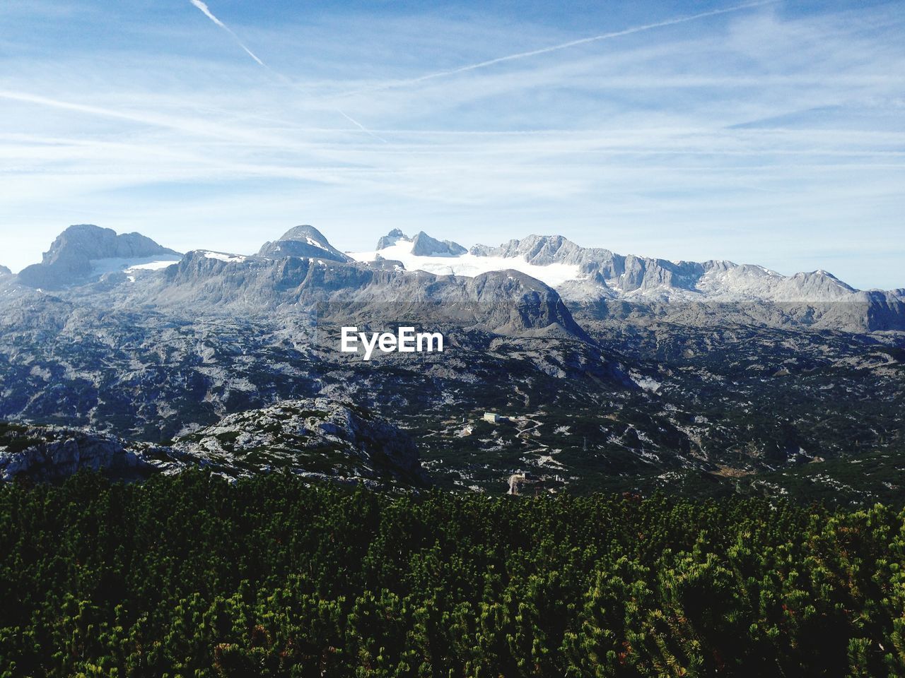 Scenic view of trees and snowcapped mountain against cloudy sky