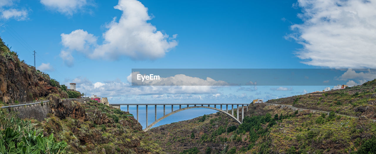 sky, cloud, bridge, nature, water, architecture, travel destinations, environment, travel, built structure, scenics - nature, landscape, mountain, panoramic, blue, transportation, tourism, plant, no people, land, beauty in nature, sea, outdoors, tree, mountain range, day, reservoir, tranquility, trip, vacation, city, holiday, tranquil scene, environmental conservation
