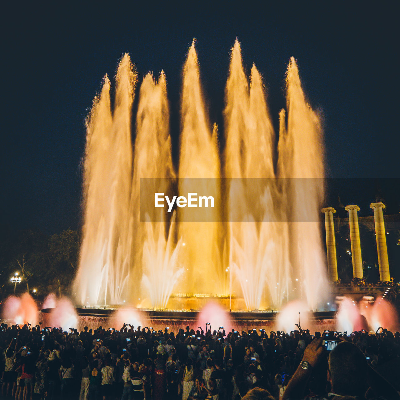 Crowd watching huge fountain against sky at night