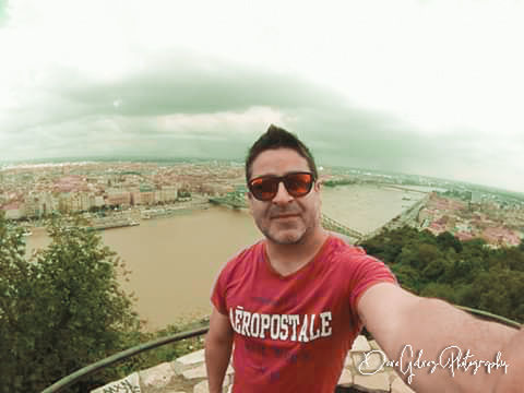 one person, portrait, sunglasses, glasses, fashion, adult, looking at camera, nature, smiling, front view, vacation, sky, day, men, architecture, t-shirt, casual clothing, happiness, lifestyles, leisure activity, waist up, water, young adult, outdoors, cloud, landscape, emotion, standing, city, copy space, built structure, communication, tree, holiday, facial hair, building exterior, land, person