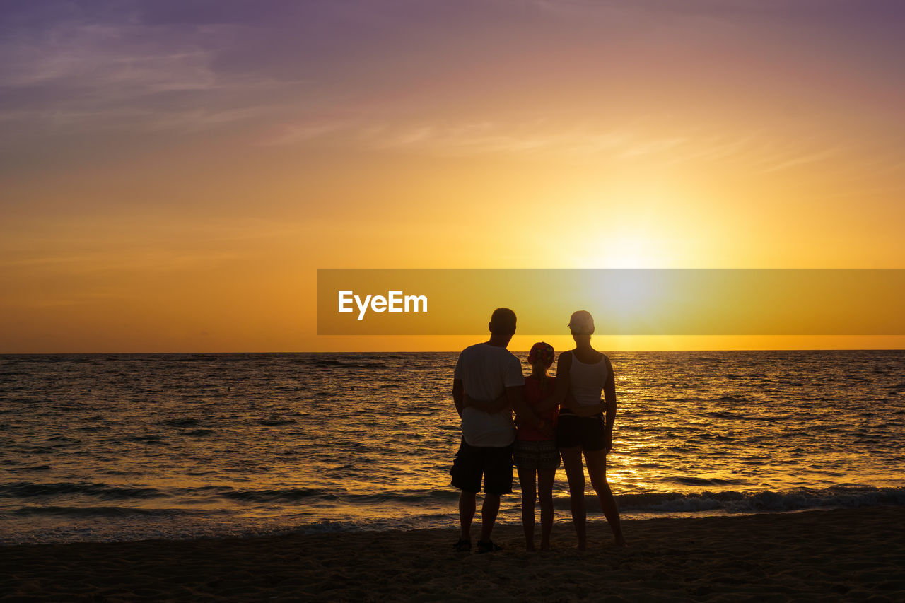 Rear view of family standing on shore at beach during sunset