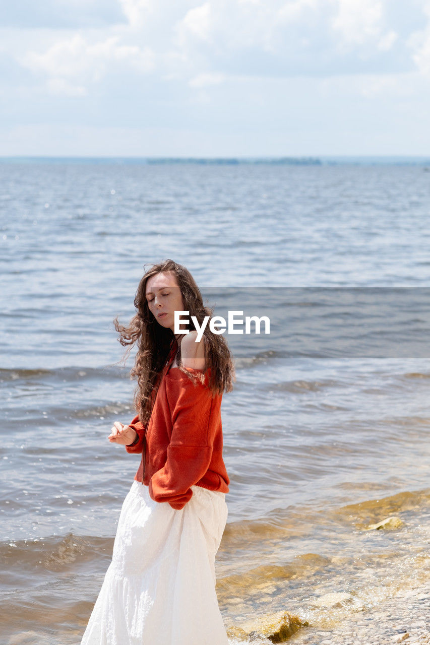 water, sea, one person, women, beach, long hair, horizon over water, sky, dress, adult, horizon, land, nature, hairstyle, standing, young adult, clothing, smiling, female, bride, happiness, beauty in nature, brown hair, emotion, wedding dress, day, leisure activity, cloud, portrait, fashion, three quarter length, shore, holiday, person, outdoors, tranquility, lifestyles, positive emotion, looking, casual clothing, full length, photo shoot, vacation, ocean, looking at camera, front view, scenics - nature, trip, coast, motion, gown