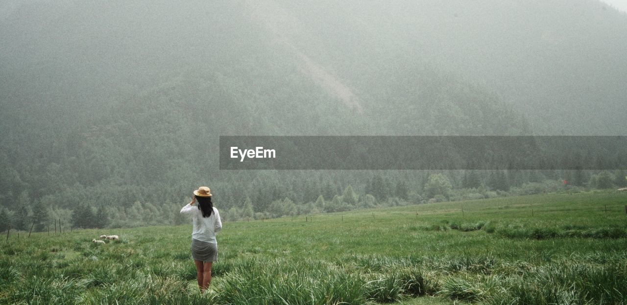 Rear view of woman standing on grassy field against mountains