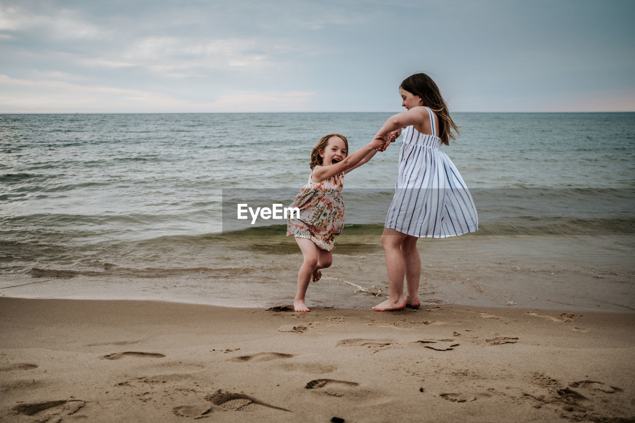 Older sister swinging younger sister on the beach at lake michigan