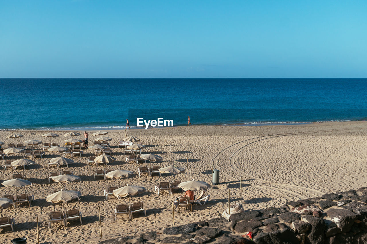 Deck chairs and parasols at beach against clear blue sky