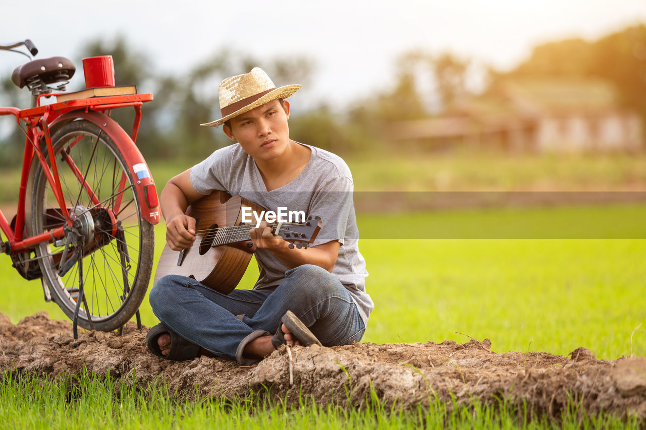 Man playing guitar while sitting by bicycle in field