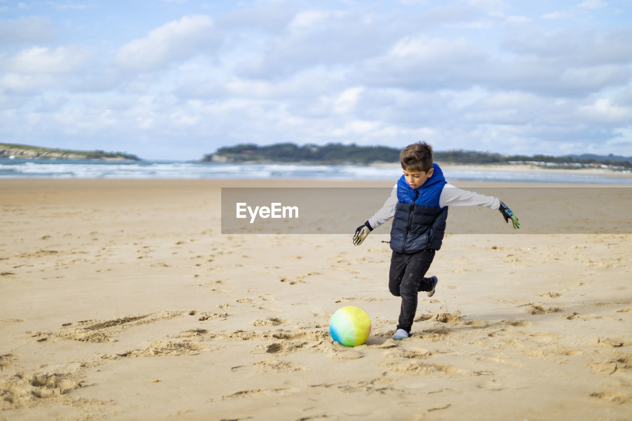 Cute boy playing with ball at shore of beach