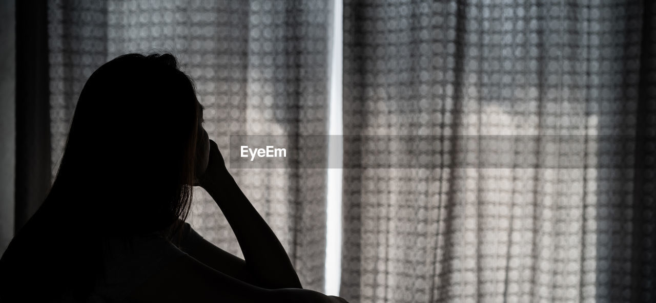 Silhouette woman sitting by curtain