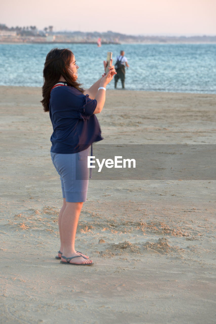 FULL LENGTH REAR VIEW OF WOMAN STANDING AT BEACH