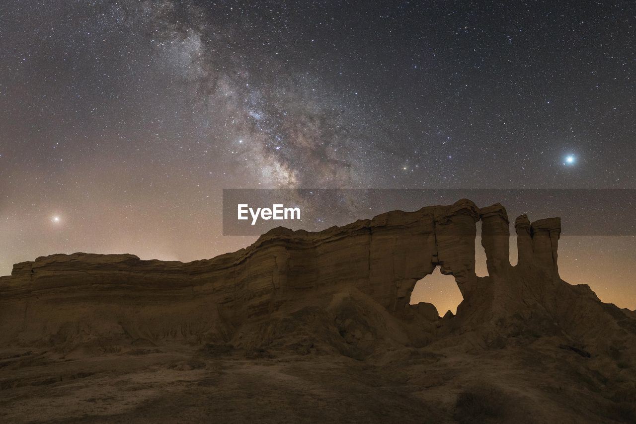 Milky way above rockcliffs .
 mars at left, jupiter at right  and saturn at the middle of milky way.