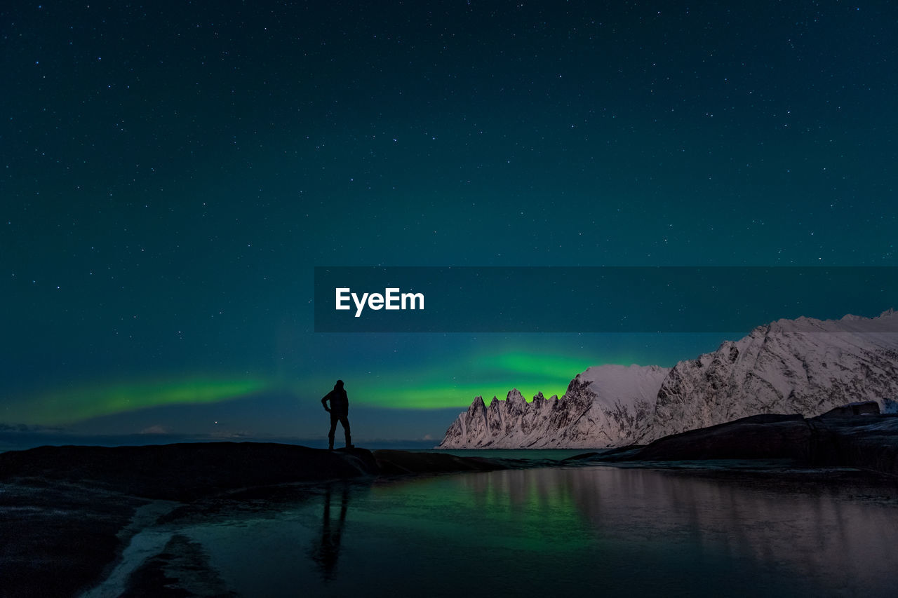 Rear view of man standing against aurora borealis at night