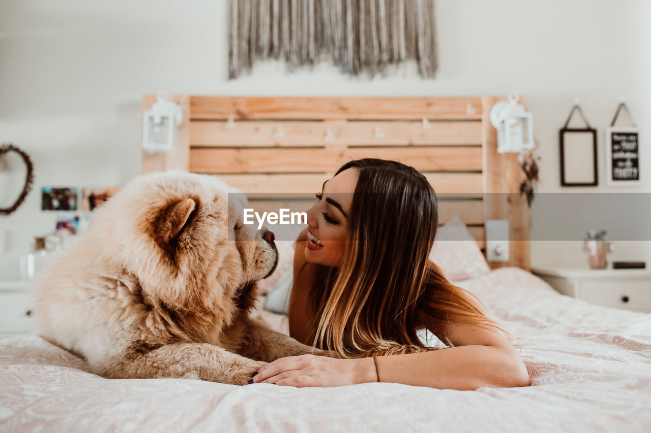 Smiling young woman lying with dog on bed at home