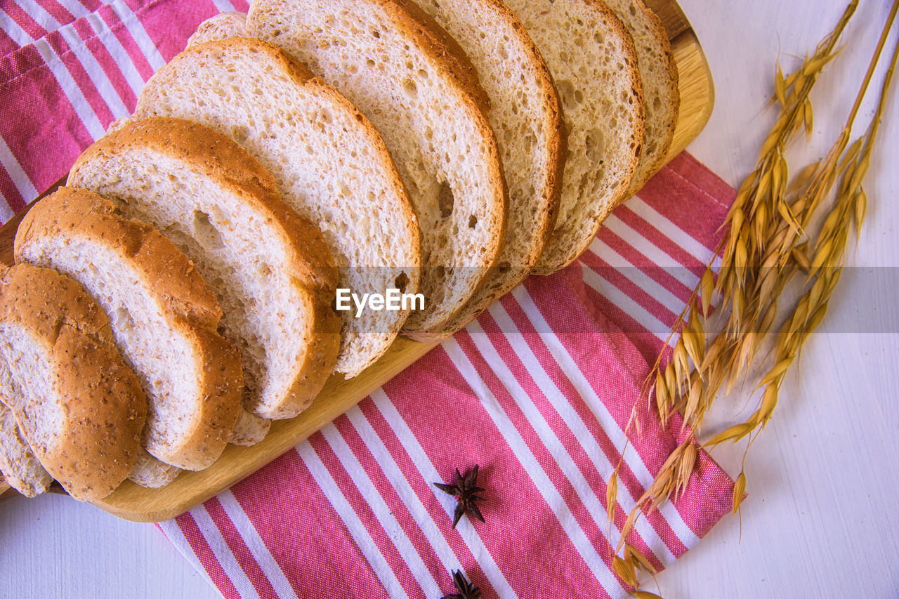 High angle view of bread slices with wheat crops on table