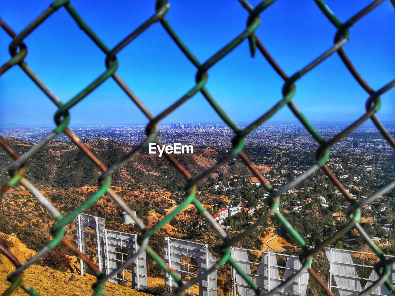 FULL FRAME SHOT OF CHAINLINK FENCE AGAINST BLUE SKY SEEN THROUGH METAL RAILING