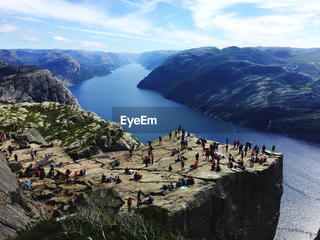 High angle view of people on cliff by lake against sky