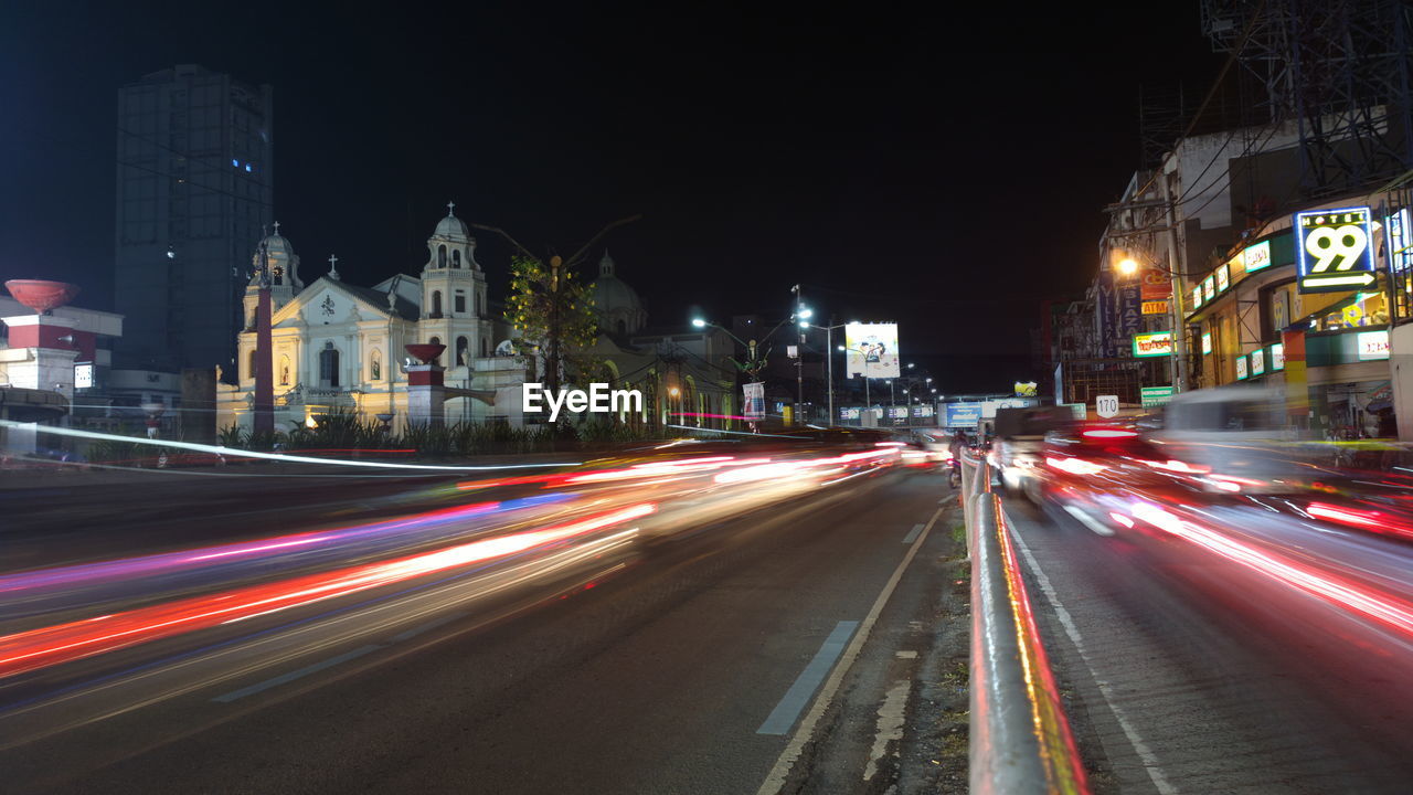 LIGHT TRAILS ON CITY STREET AGAINST ILLUMINATED BUILDINGS