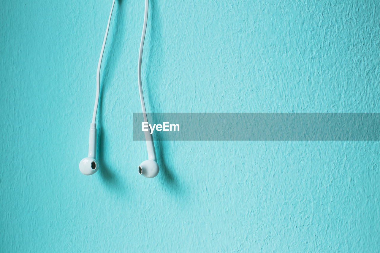 Close-up of in-ear headphones against blue wall