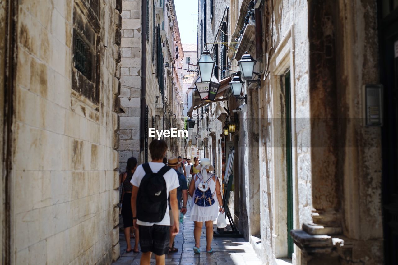 REAR VIEW OF PEOPLE WALKING ON STREET BY BUILDINGS