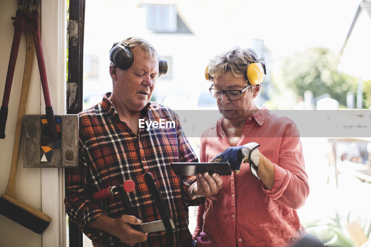 Senior couple discussing over digital tablet while standing at workshop doorway