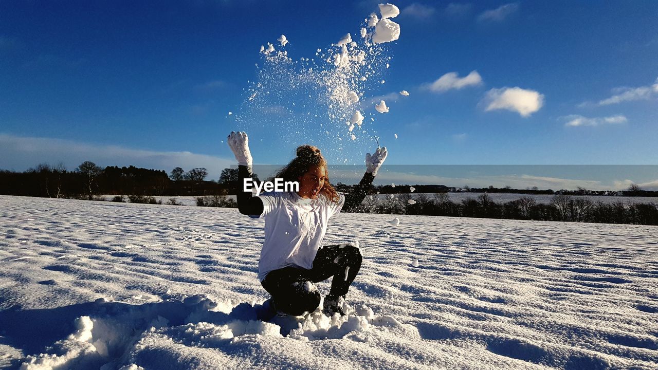 BOY PLAYING WITH SNOW ON FIELD AGAINST SKY DURING WINTER
