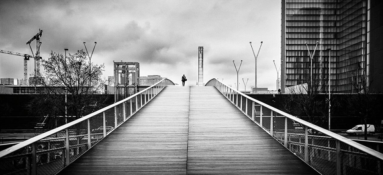 Silhouette man walking on bridge by building in city