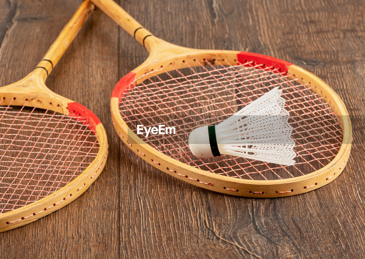 White badminton shuttlecock and two wooden badminton rackets on a wooden background.