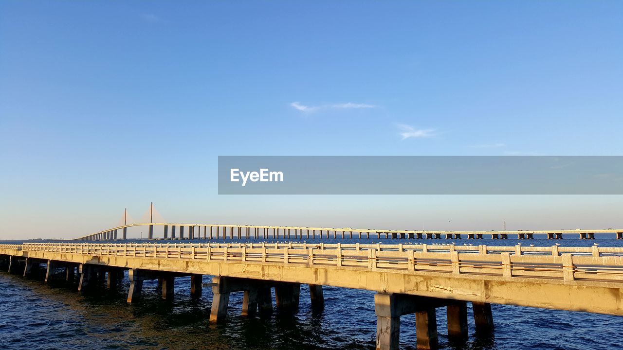 Silhouette pier over river against blue sky
