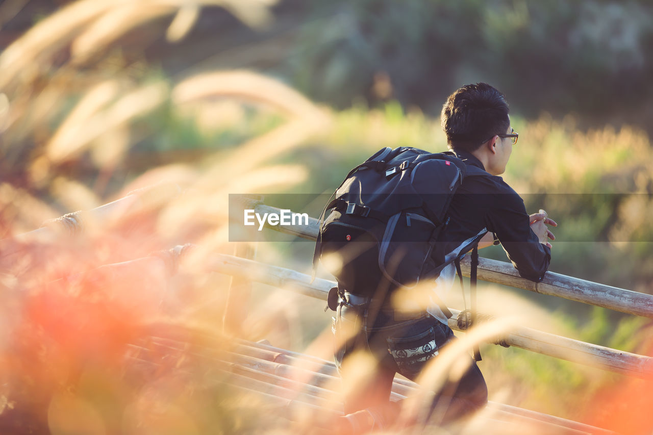 Thoughtful backpacker looking away while standing by fence