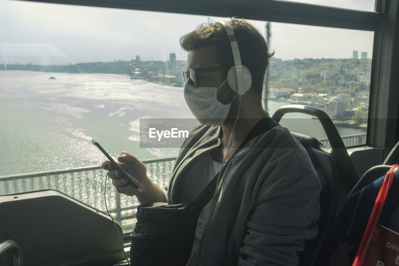 Man wearing mask using smart phone while sitting in train