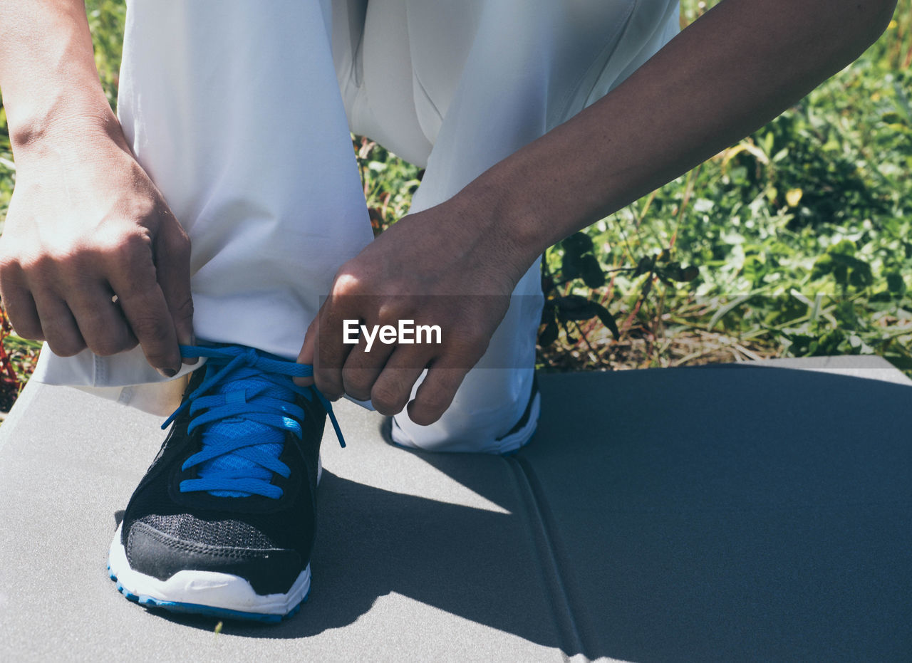 Low section of woman tying shoelace on field against clear sky